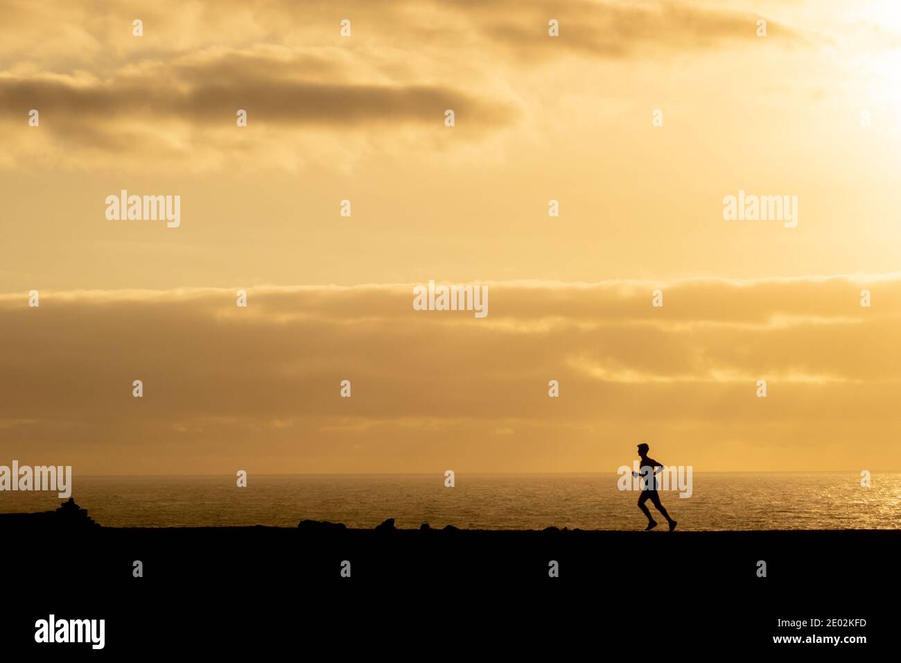 Silhouette di un uomo irriconoscibile che corre di fronte al mare al tramonto a Lanzarote, Isole Canarie, Spagna. Assistenza sanitaria e esercizio all'aperto concep. Foto Stock