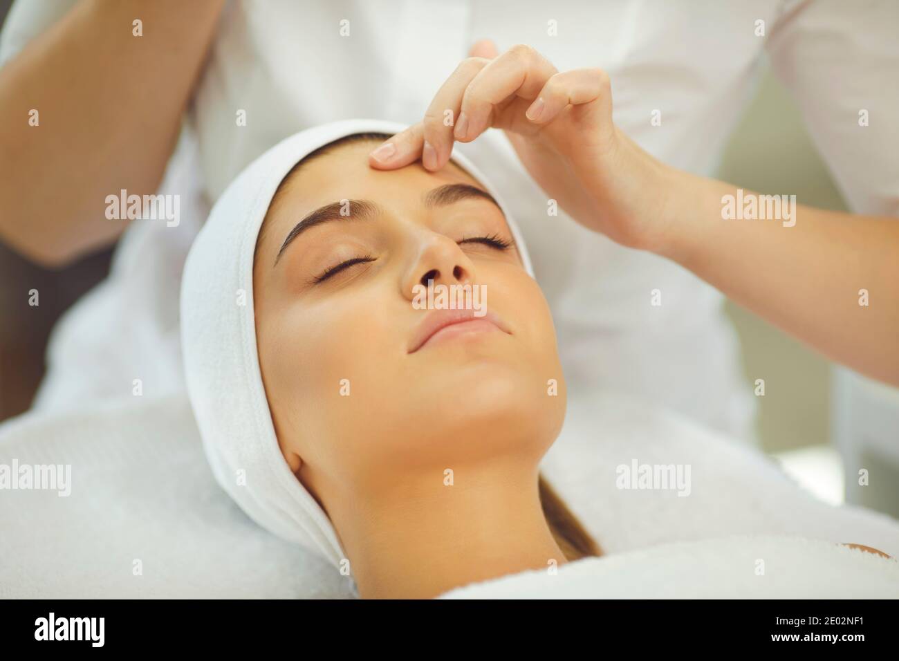 Mani di cosmetologist che controllano l'elasticità della pelle o che fanno la pulizia del viso per una giovane donna rilassante Foto Stock