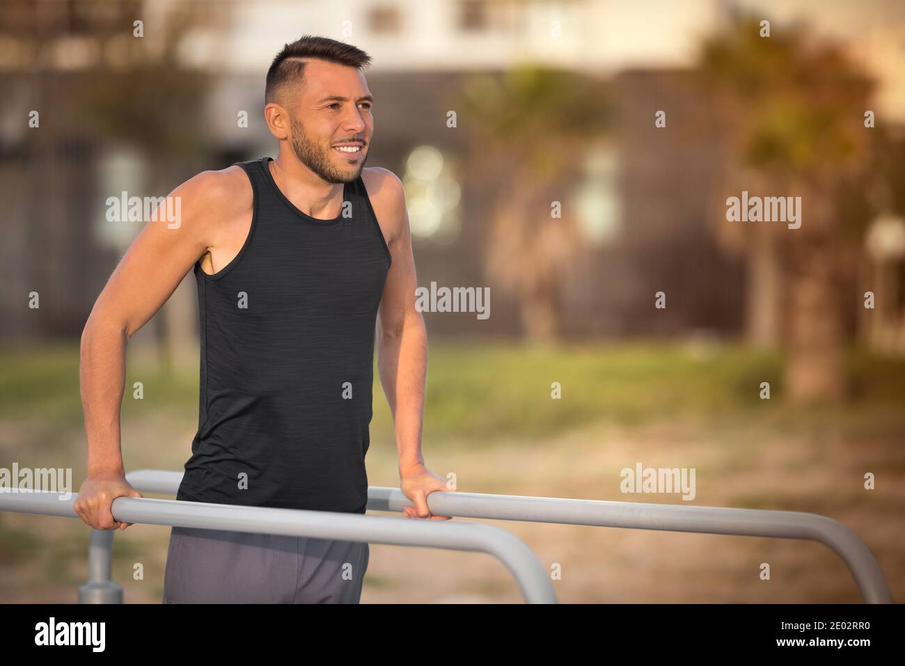 Giovane uomo sportivo che fa i triceps tuffa sulle barre parallele all'aperto. Fare esercizi su barre parallele nel parco Foto Stock