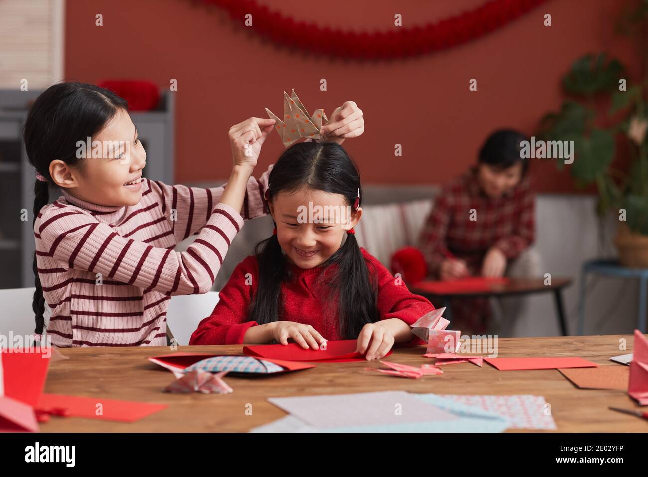 Ritratto medio di due ragazze cinesi che si divertono mentre Preparazione di decorazioni in carta colorata per la festa lunare di Capodanno Foto Stock