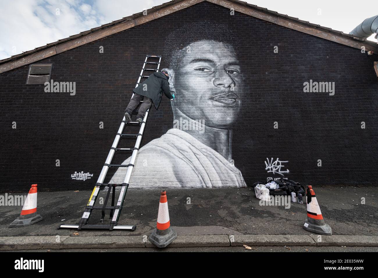 L'artista di strada Akse, si trova di fronte al murale della star del calcio Marcus Rashford. Foto Stock