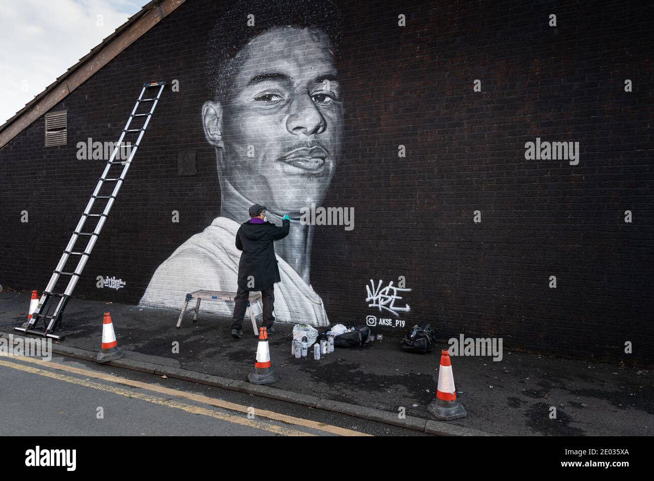 L'artista di strada Akse, si trova di fronte al murale della star del calcio Marcus Rashford. Foto Stock