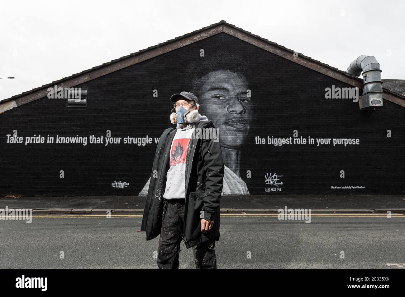 L'artista di strada Akse, si trova di fronte al murale della star del calcio Marcus Rashford. Foto Stock