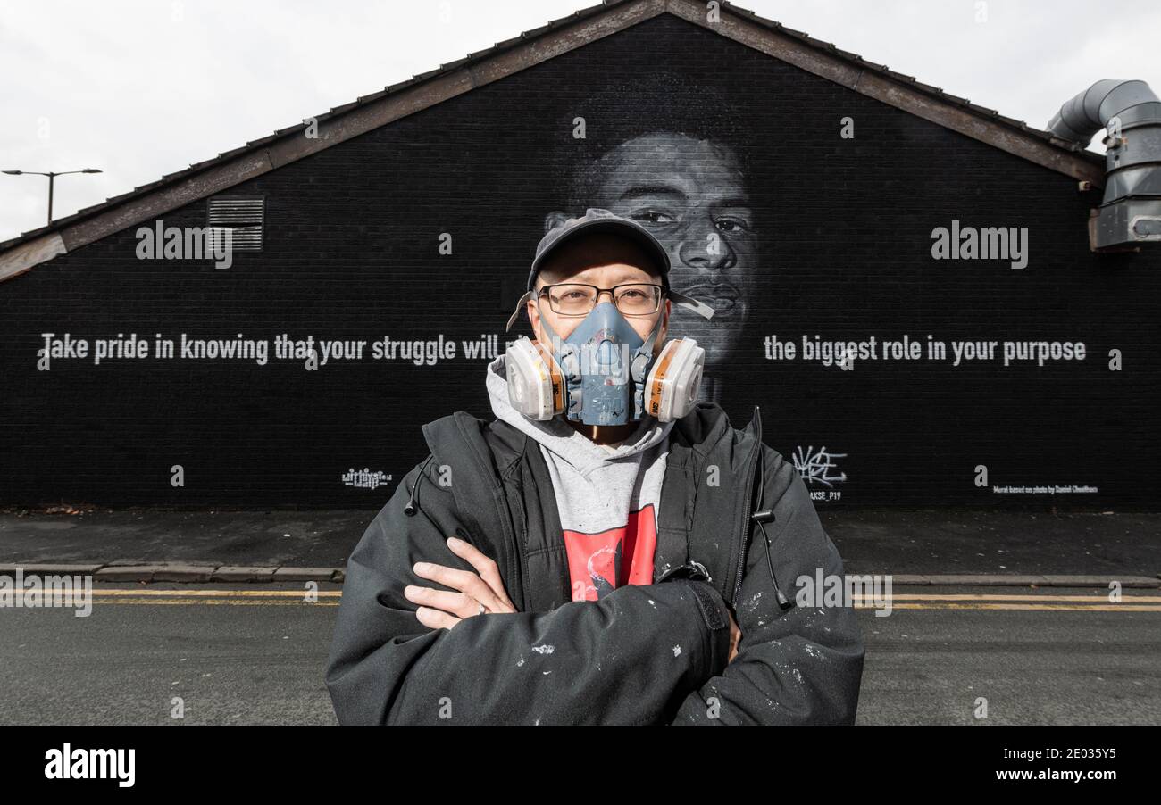 L'artista di strada Akse, si trova di fronte al murale della star del calcio Marcus Rashford. Foto Stock