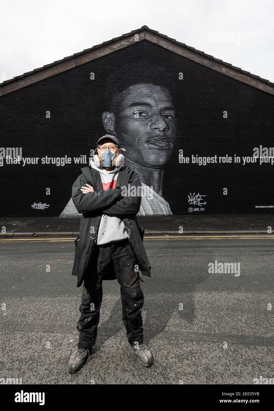 L'artista di strada Akse, si trova di fronte al murale della star del calcio Marcus Rashford. Foto Stock