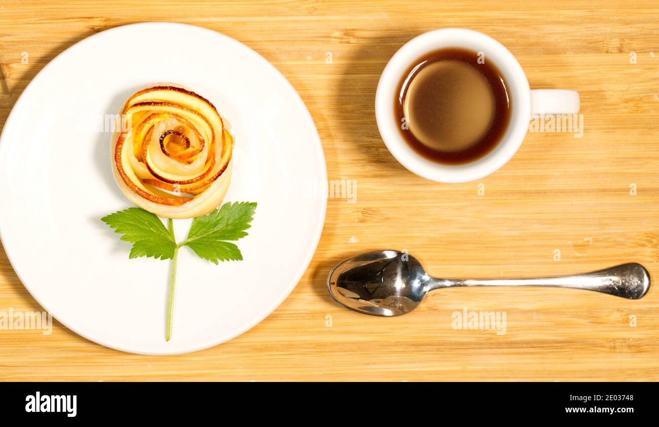 Tazza di caffè, gustosa pasticceria fatta in casa a forma di rosa di mele su un tavolo di legno, colazione nutriente, vista dall'alto Foto Stock