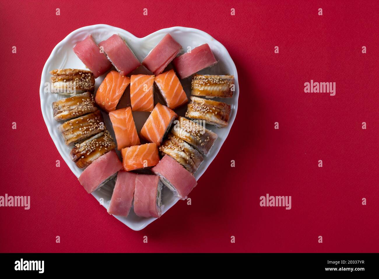 Sushi Set di salmone, tonno e anguilla con formaggio philadelphia in piatto come cuore su sfondo rosso. Concetto di cibo per San Valentino. Vista dall'alto Foto Stock