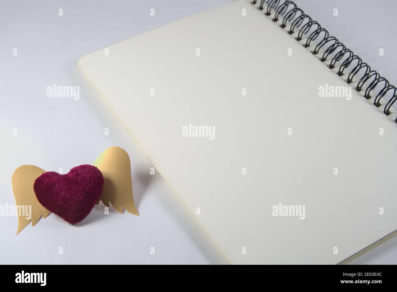 Notebook vuoto con rilegatura a spirale e decorazioni a forma di cuore rosso su scrivania bianca, spazio per la copia Foto Stock