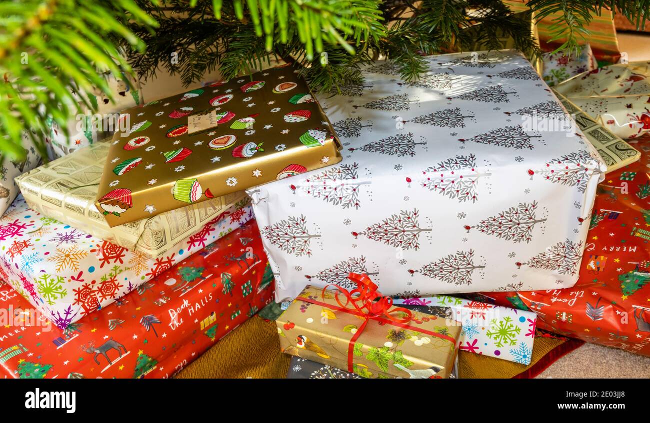 Regali di Natale avvolti in tradizionale festivo colorato carta da imballaggio accatastato Sotto un albero di Natale Foto Stock