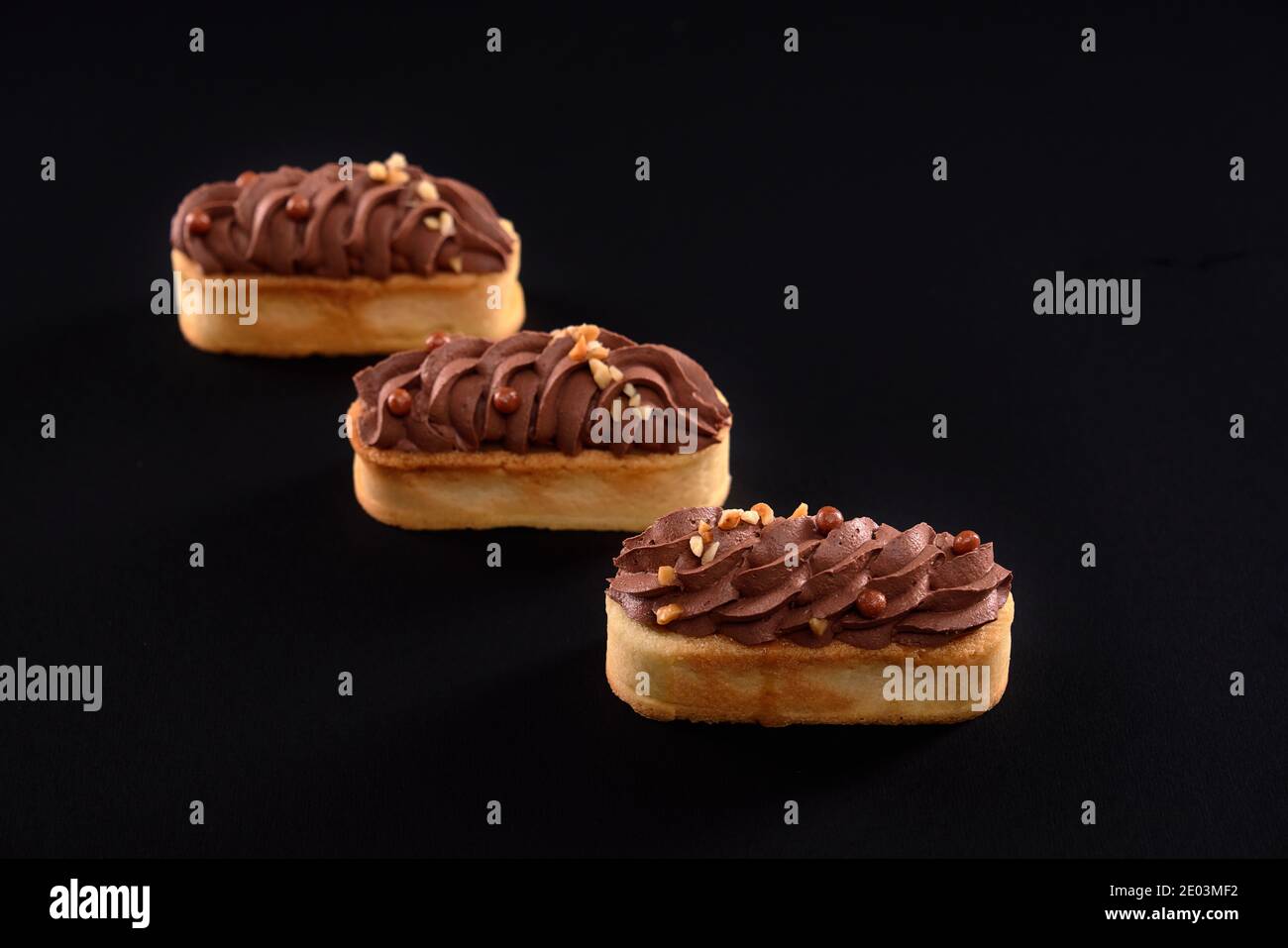 Tre dolci appena fatti in casa, isolati su sfondo nero. Biscotti shortbread con panna di cioccolato marrone montata mascarpone. Concetto di dolci, industria alimentare. Foto Stock