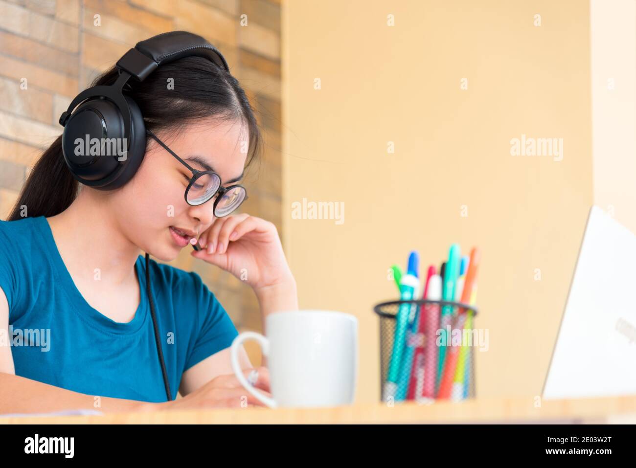 Asian adolescente studente ragazza con uno spettacolo cuffia scrivere a. nota nel notebook parlare in un microfono utilizzando un computer portatile studio online della scuola d Foto Stock