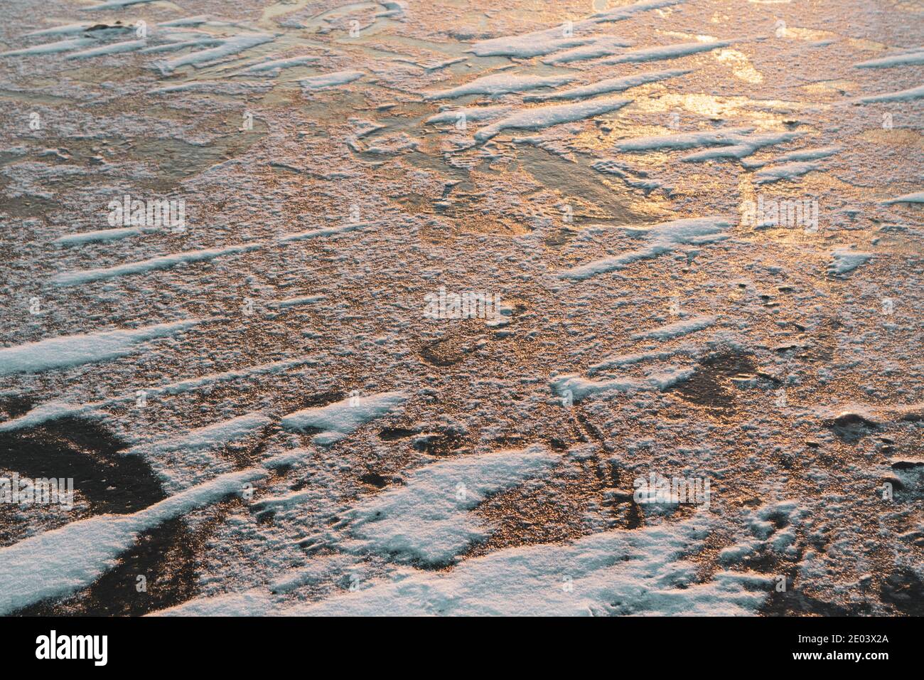 Ghiacciato freddo profondo lago superficie coperta di neve primo piano scintillante su caldo sfondo arancione con luce del tramonto Foto Stock