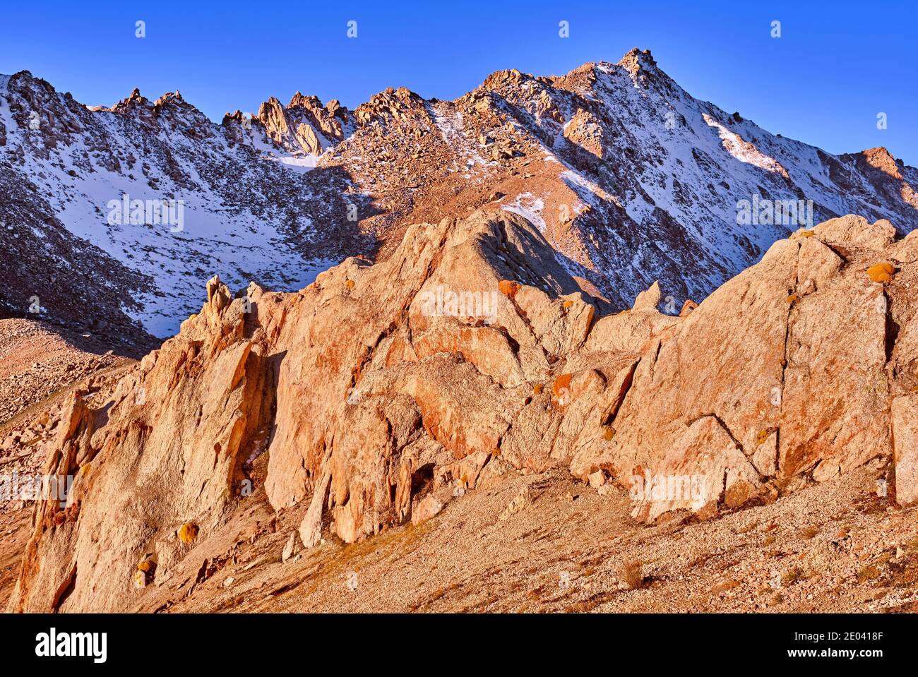 Rocce con licheni sullo sfondo di maestosa vetta di montagna nella morbida luce del mattino con chiaroscuro contro il cielo blu Foto Stock