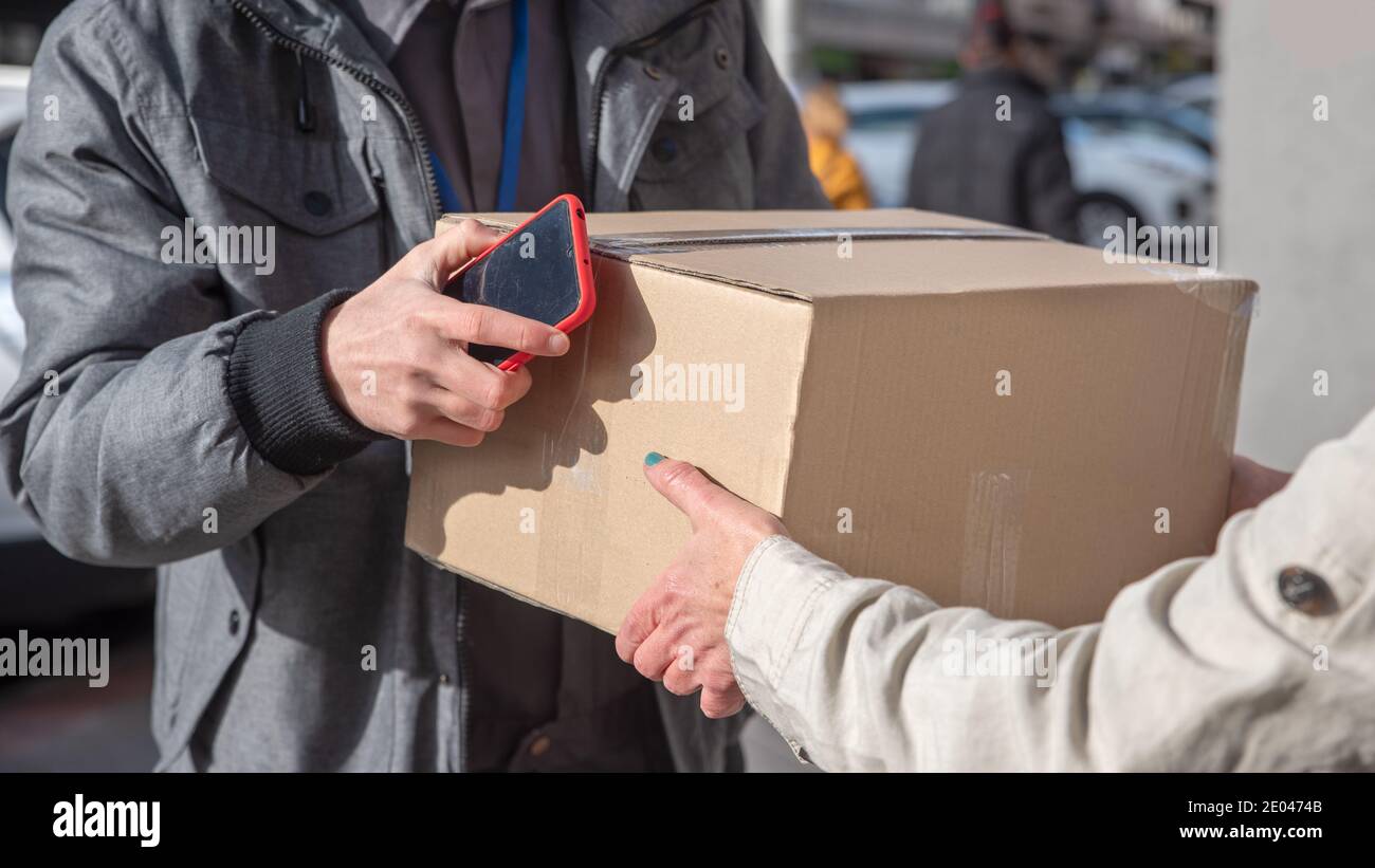 Uomo di consegna con il telefono cellulare in mano mani su un box alla donna Foto Stock