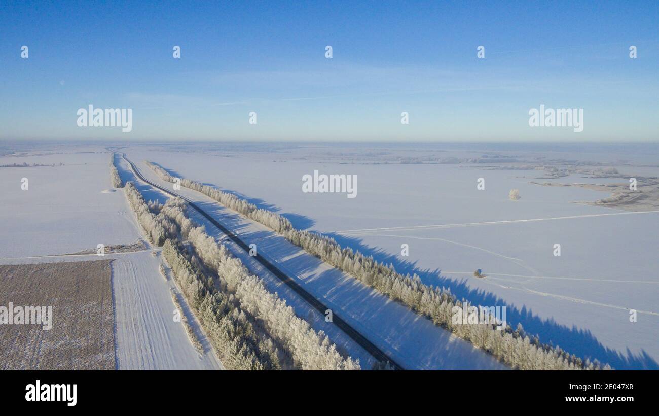 Strada invernale lungo i campi tra le città vista aerea da un drone. Paesaggio invernale da un drone. Vista invernale sulla strada da un drone Foto Stock