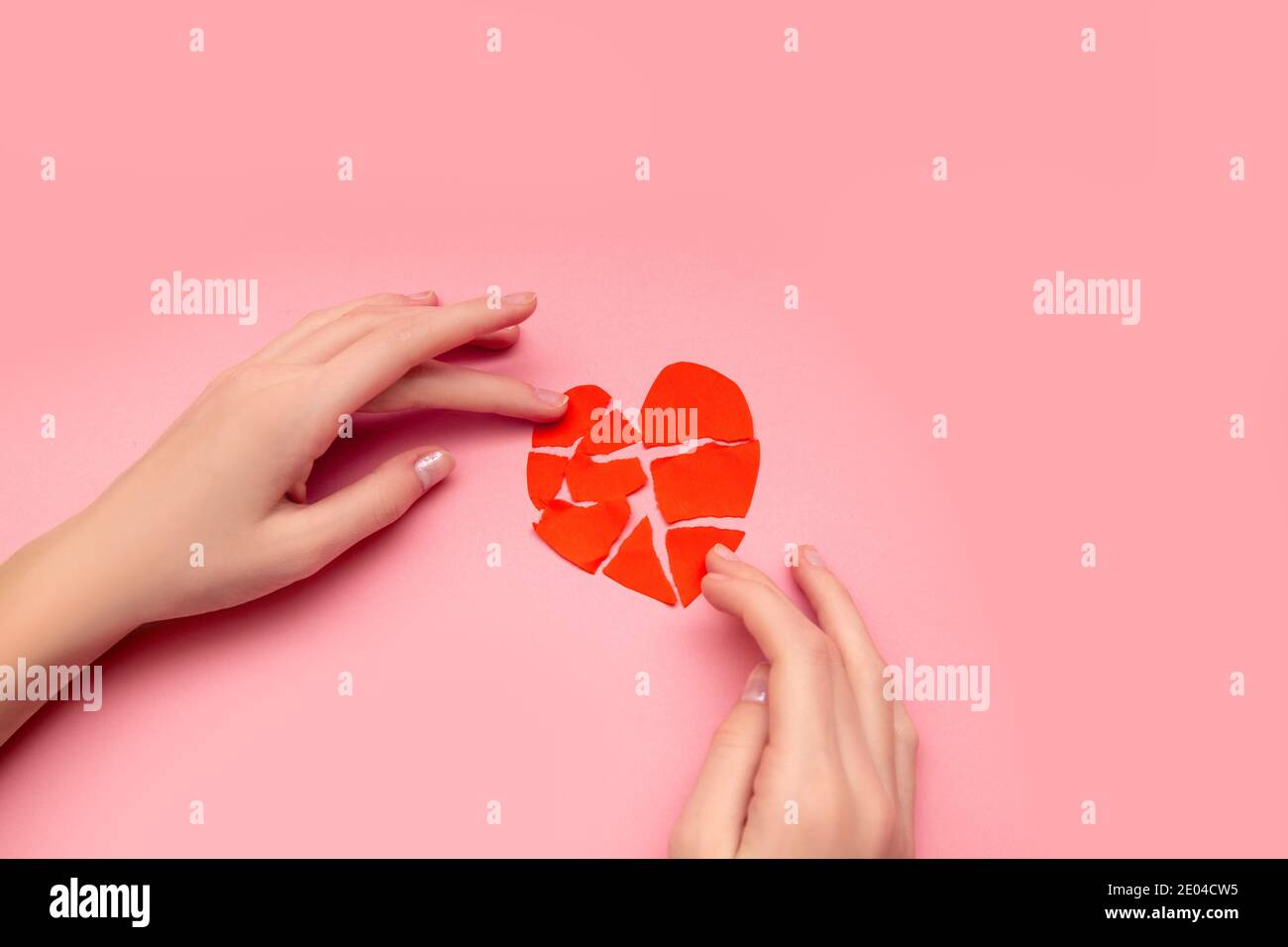 Mani femminili incollando insieme cuore rotto, pezzi di rosso-valentina strappato su sfondo rosa. Concetto di delusione nell'amore, salvezza del relazionish Foto Stock