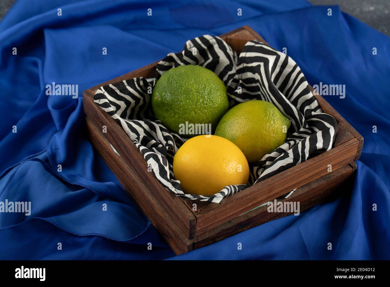 Un cesto di legno con tre limoni su un panno blu Foto Stock