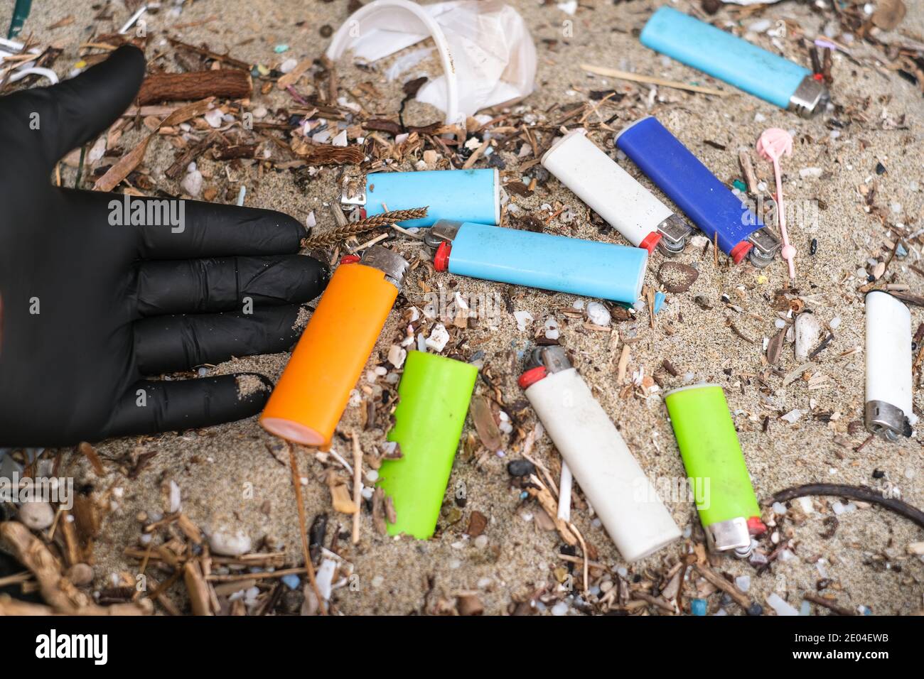 Uomo che raccoglie micro accendini di plastica rifiuti sulla costa sporca dell'oceano ecosistema, inquinamento della natura Foto Stock
