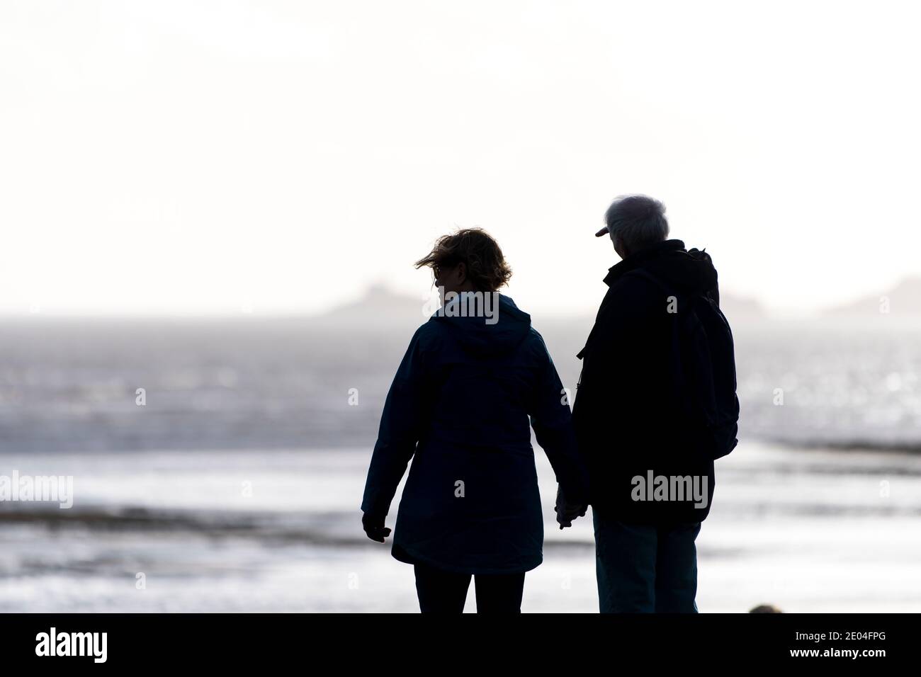 Un uomo e una donna dalle silhouette tengono le mani su una spiaggia. Foto Stock