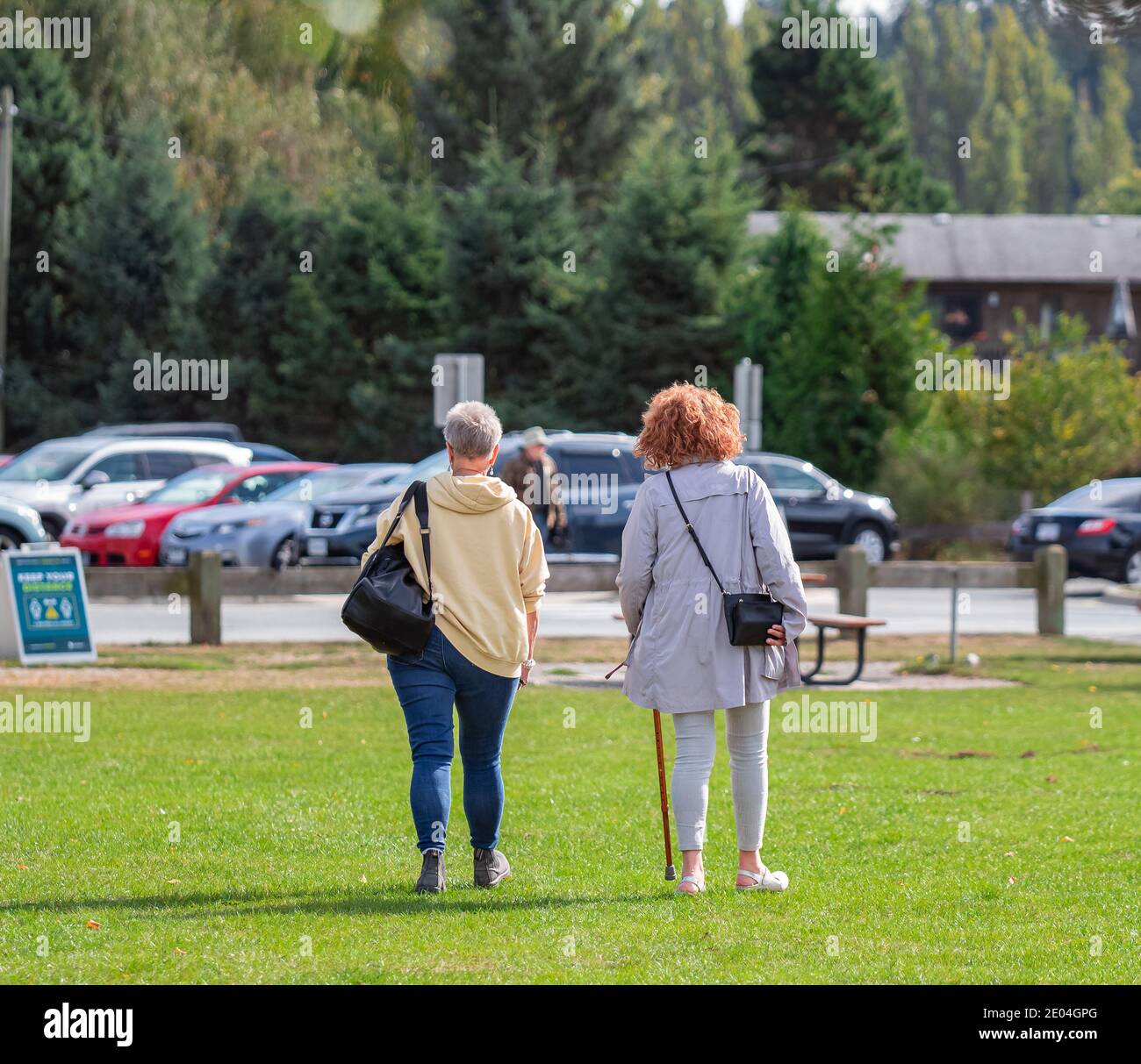Vista posteriore di due donne che camminano e parlano in un parco una soleggiata giornata d'autunno. Messa a fuoco selettiva, vista strada, foto di viaggio. Foto Stock