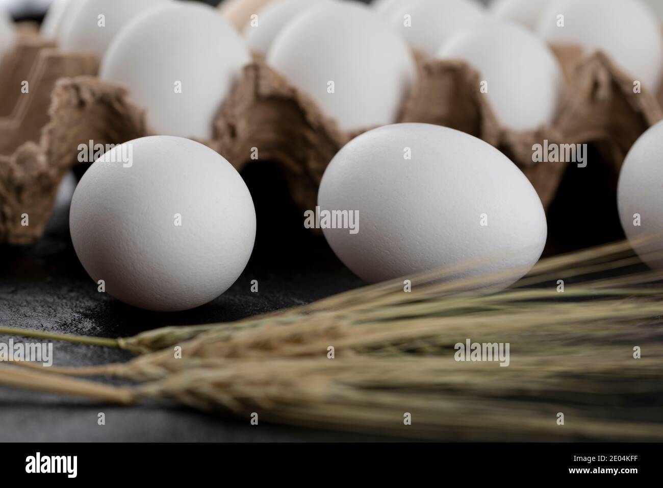 Contenitore di uova bianche e spighe di grano su nero sfondo Foto Stock