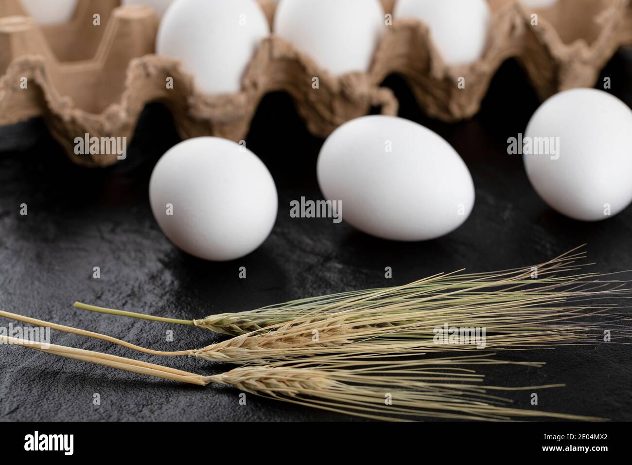Contenitore di uova bianche e spighe di grano su nero sfondo Foto Stock