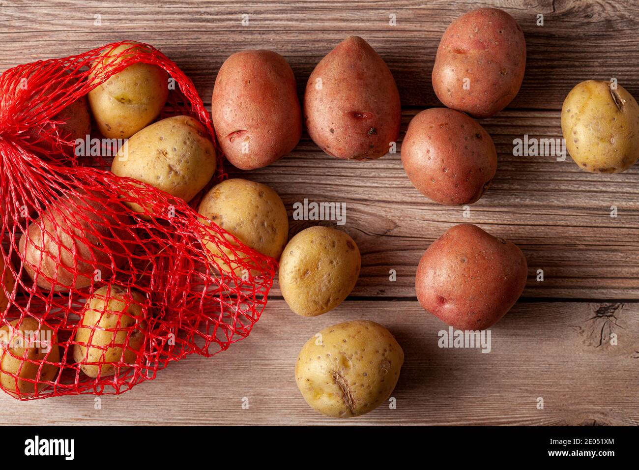 Immagine ravvicinata piatta con un sacco di patate in mesh rossa con patate biologiche crude rosa e gialle su sfondo di legno. Un alimento versatile per la natura morta Foto Stock