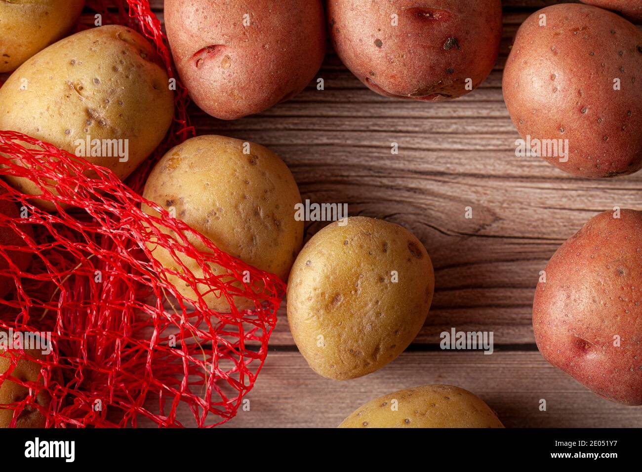 Immagine ravvicinata piatta con un sacco di patate in mesh rossa con patate biologiche crude rosa e gialle su sfondo di legno. Un alimento versatile per la natura morta Foto Stock