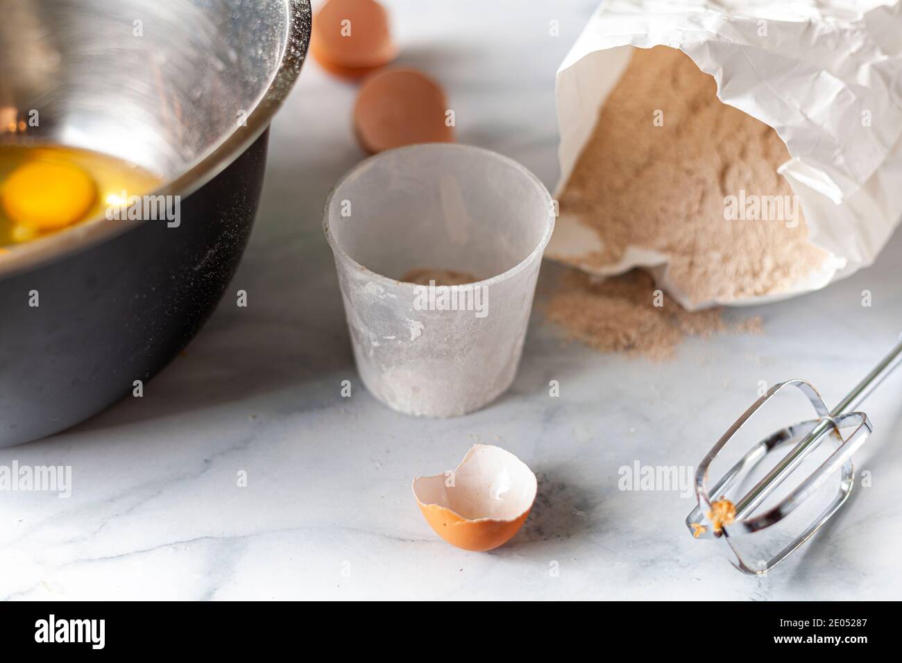 Pasta in fase di preparazione su piano cucina in marmo con un sacchetto di carta di farina integrale, gusci d'uovo rotti, misurino e accessorio miscelatore visto. R Foto Stock