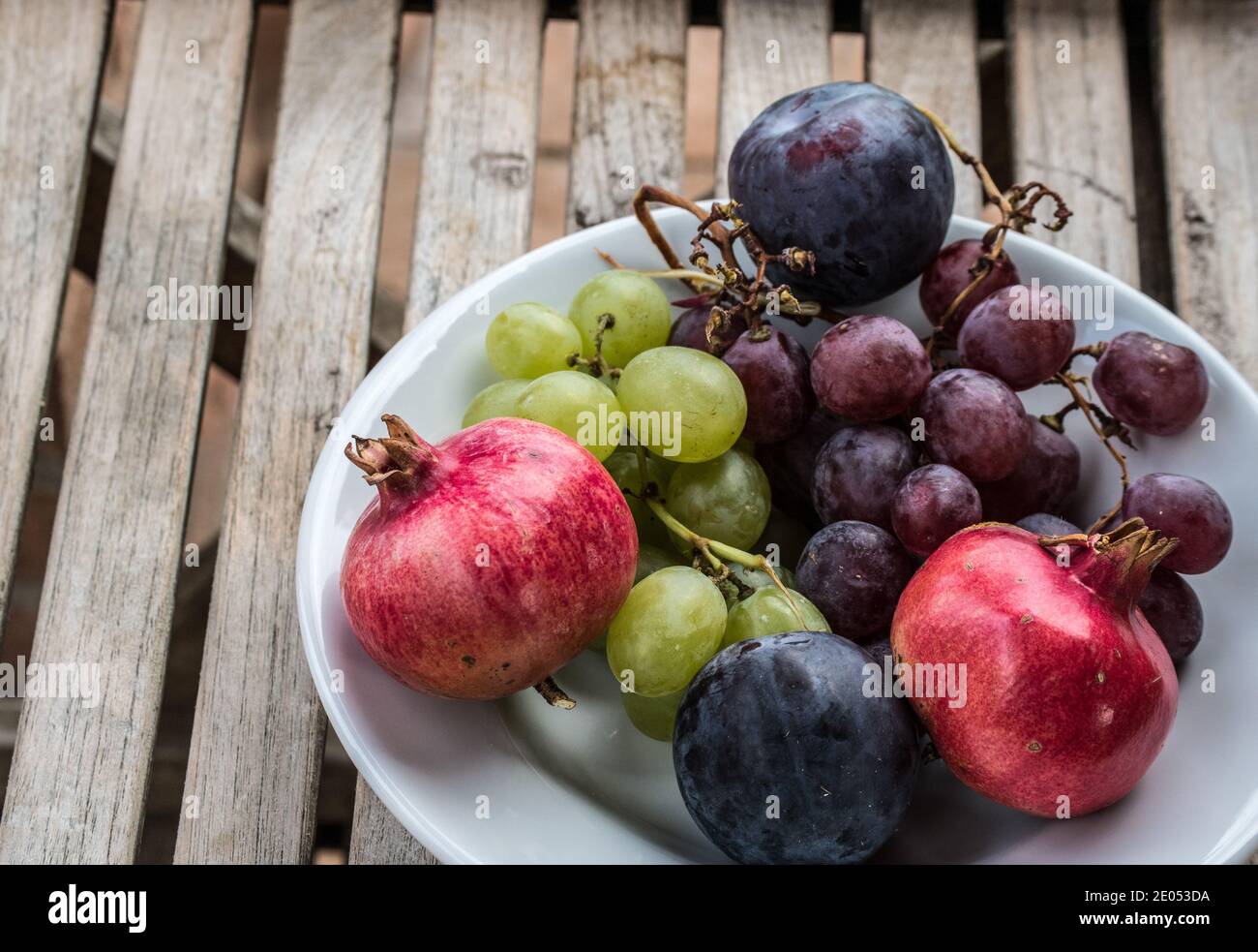 Ciotola bianca ripiena di frutta fresca biologica proveniente da un giardino rustico in Italia, uva, melograno e prugne Foto Stock