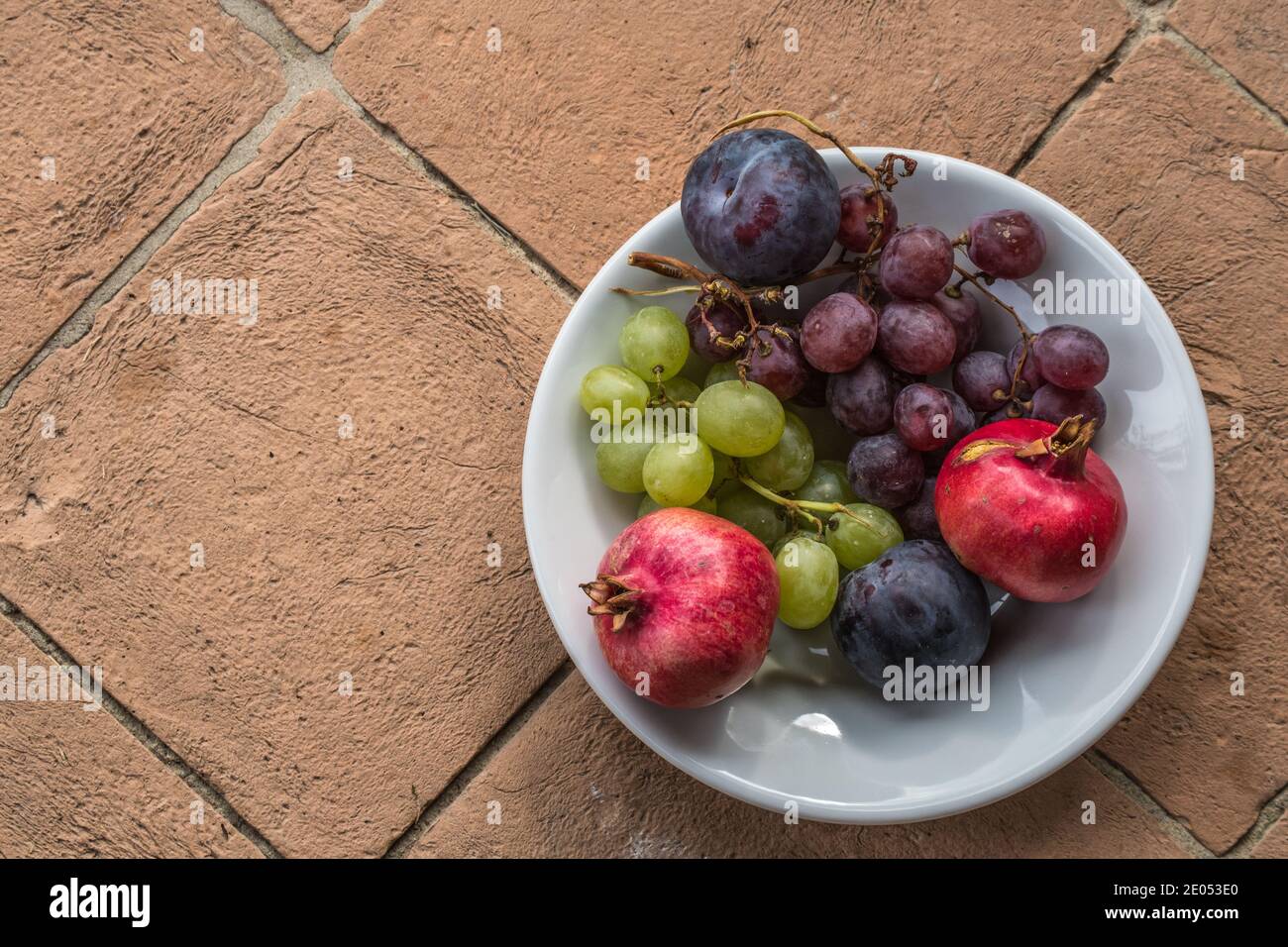 Ciotola bianca ripiena di frutta fresca biologica proveniente da un giardino rustico in Italia, uva, melograno e prugne Foto Stock
