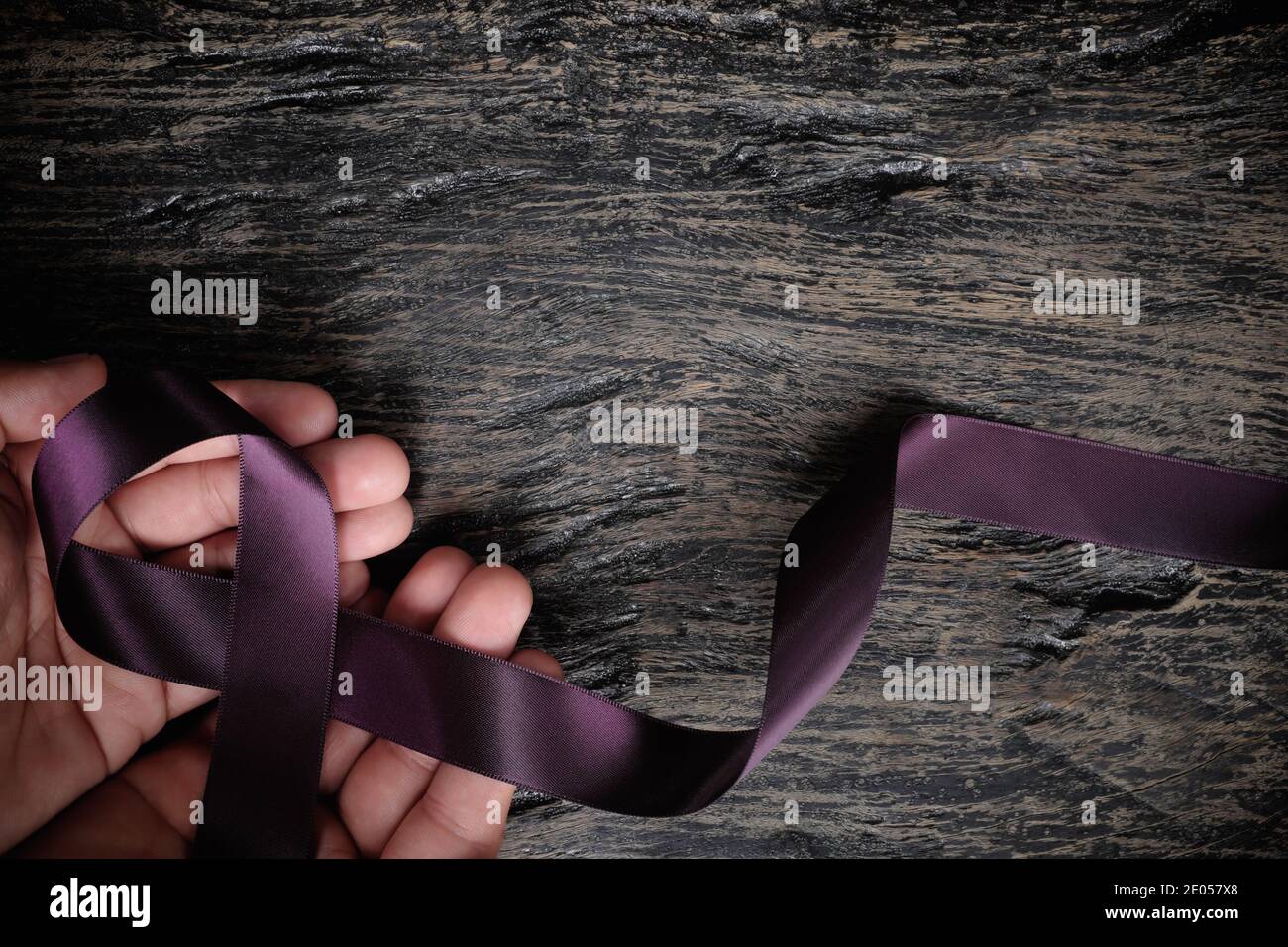 Vista dall'alto della mano maschio che tiene il nastro viola su sfondo di legno con spazio di copia. Cancro pancreatico, epilessia, leiomiosarcoma, lupus, Alzheimer Foto Stock