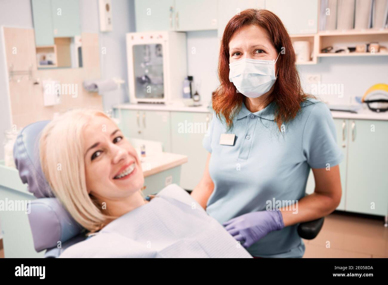 Dentista femminile seduto accanto alla paziente gioiosa femmina con bretelle sui denti. Donna che ha appuntamento con ortodontista. Concetto di odontoiatria, cura dentale e trattamento ortodontico. Foto Stock