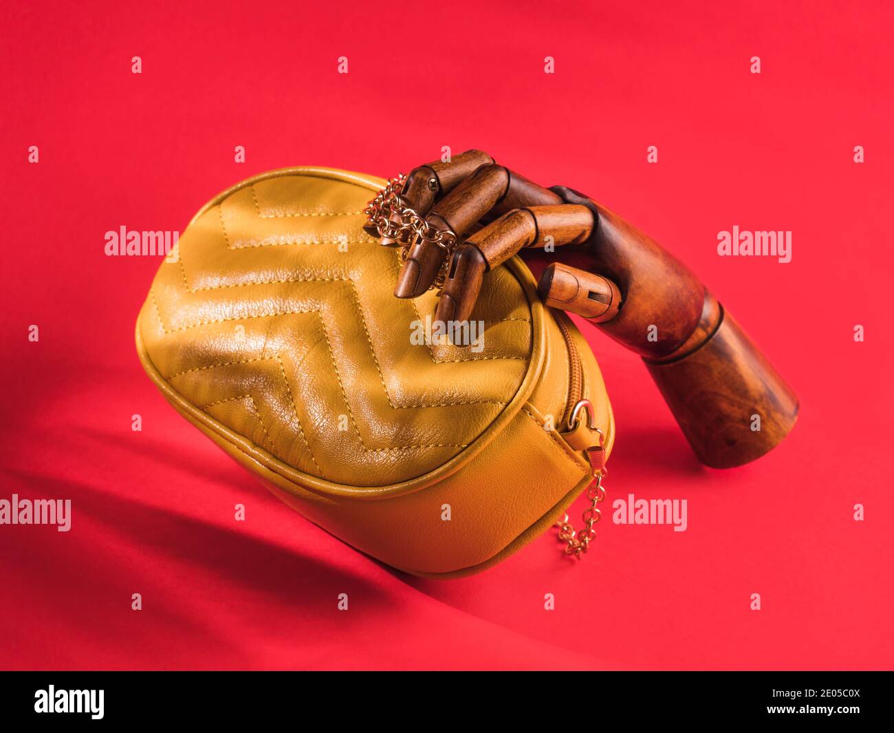 Mano di legno che tiene la borsa di pelle gialla sul rosso Foto Stock
