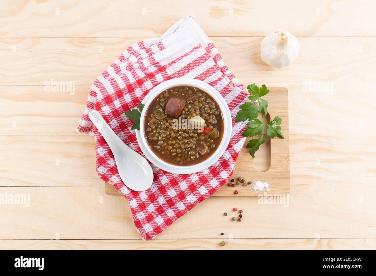 Piatto tradizionale spagnolo di stufato di lenticchie con chorizo e patate, su base di legno chiaro. Composizione di posa piatta. Foto Stock