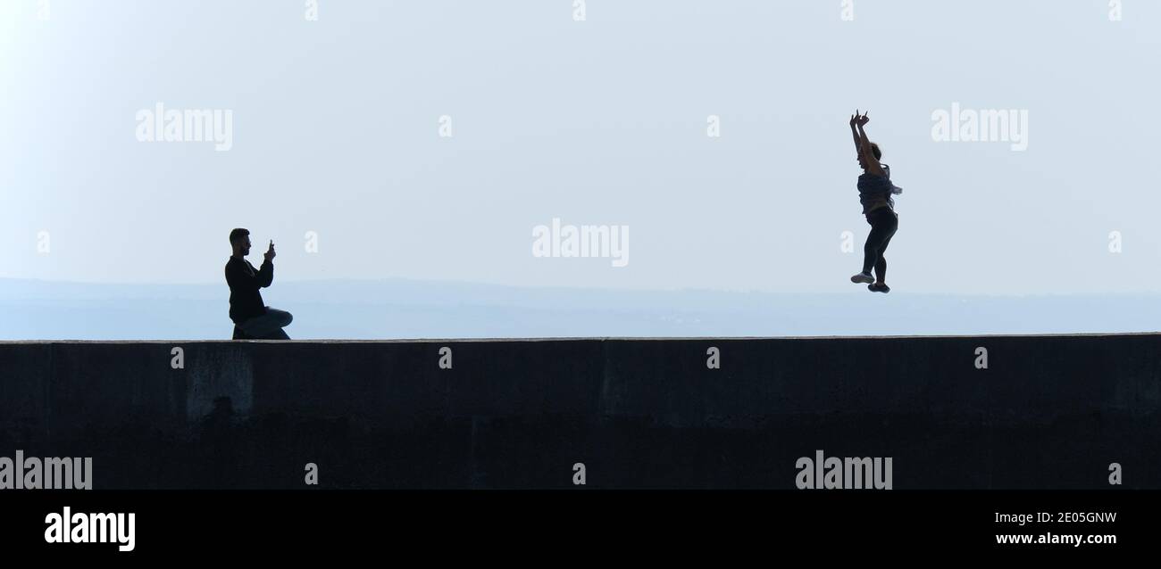 Silhouette di fotografo maschile fotografando femmina facendo un salto stellare con la sua lingua fuori. Stato Instagram o Facebook. Foto Stock