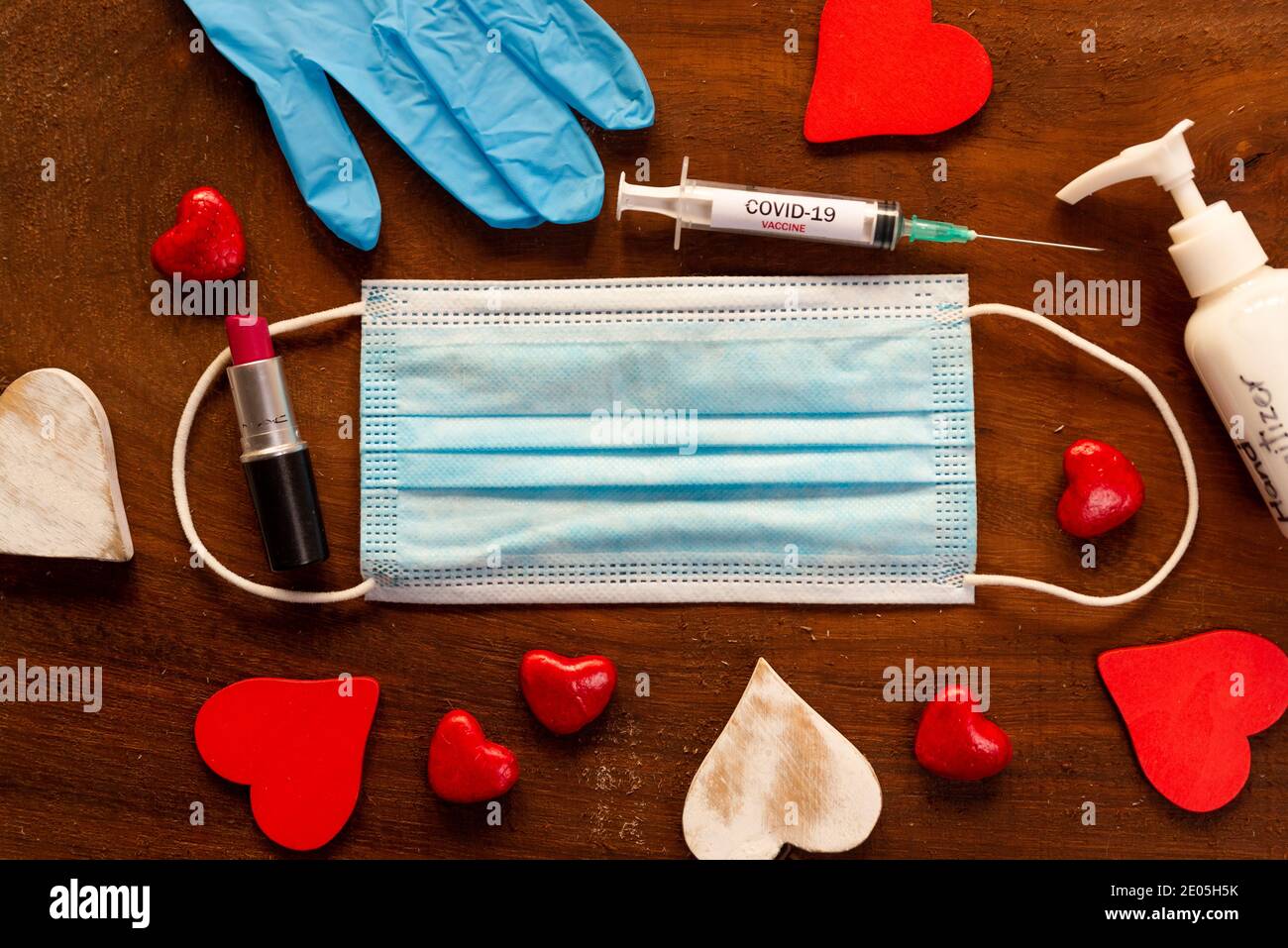 il concetto di igiene diurna di covid valentine. maschera facciale con cuori rossi su fondo di legno. vista dall'alto di disinfettante per le mani e rossetto e siringa per le vacanze Foto Stock