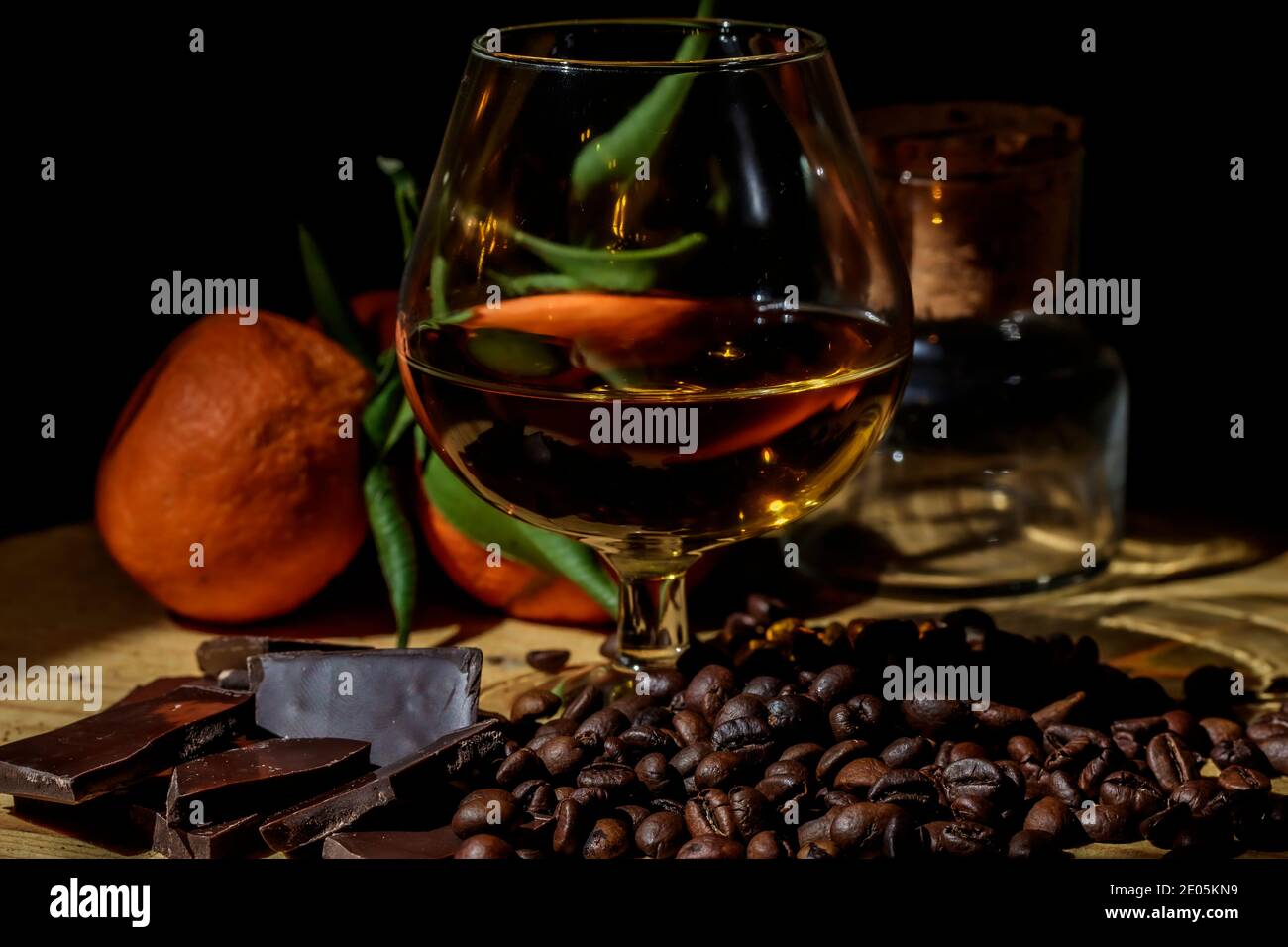 Bicchiere di brandy su tavolo di legno con cioccolato, caffè e mandarini stretti. Foto Stock