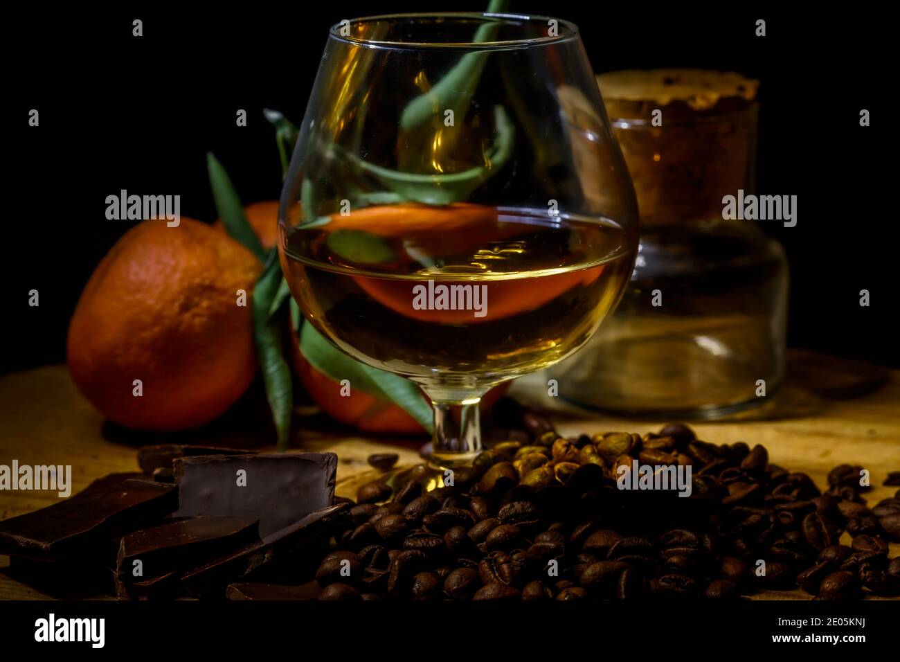 Bicchiere di brandy su tavolo di legno con cioccolato, caffè e mandarini stretti. Foto Stock