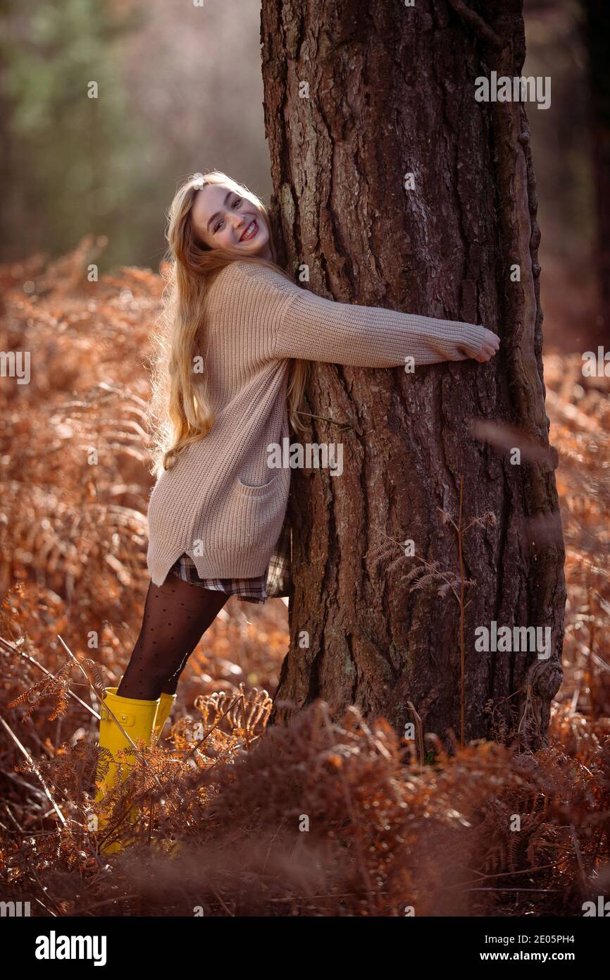 Un giovane felice attraente donne (20) abbracca un grande albero in un ambiente autunnale in un modo divertente e attento. Foto Stock