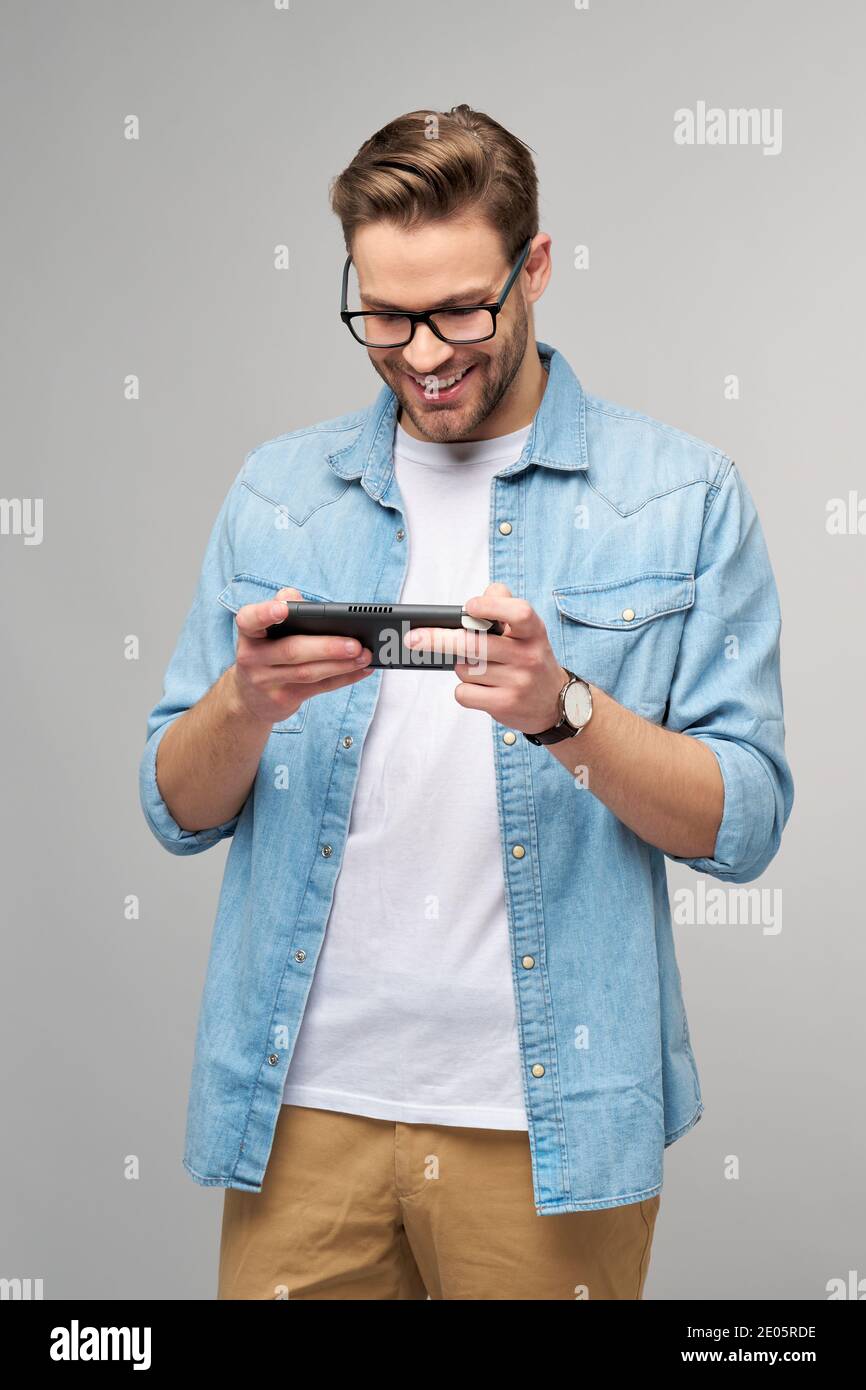 Giovane uomo a mano che gioca con un videogioco portatile in piedi sfondo grigio Foto Stock