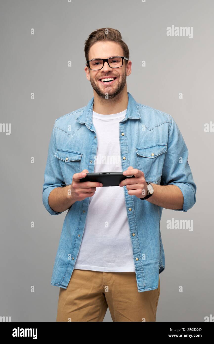 Giovane uomo a mano che gioca con un videogioco portatile in piedi sfondo grigio Foto Stock