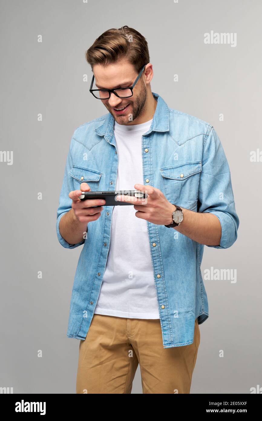 Giovane uomo a mano che gioca con un videogioco portatile in piedi sfondo grigio Foto Stock