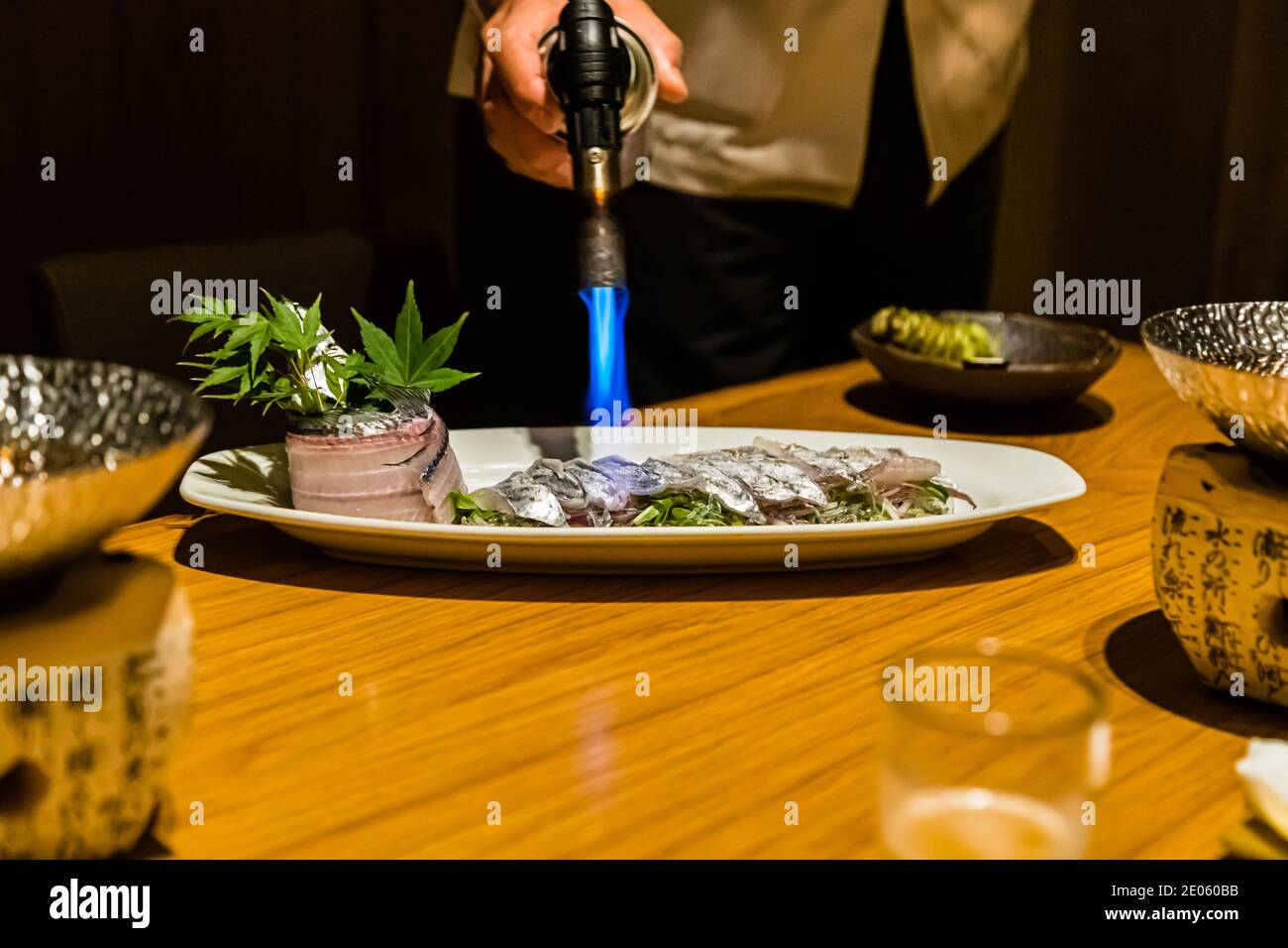 Uno chef fa rosolare la pelle di un rotolo di pesce guarnito con una foglia d’acero direttamente al tavolo utilizzando un fiammeggiatore. Ristorante a Shizuoka, Prefettura di Shizuoka, Giappone. Foto Stock