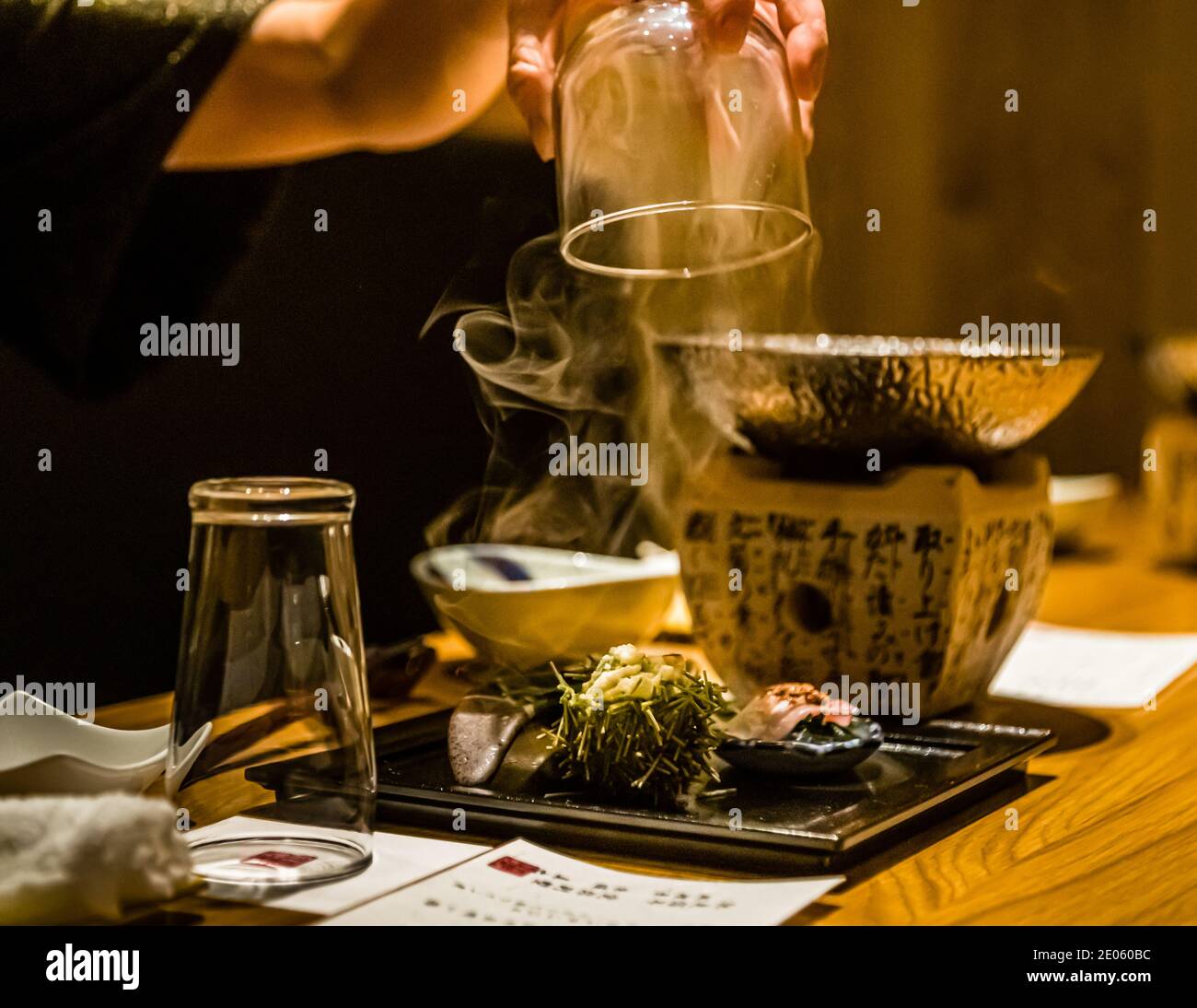 Un cameriere solleva un bicchiere da un piatto di pesce fumante. Accanto c’è un contorno artisticamente disposto di erbe e alghe. Ristorante a Shizuoka, Prefettura di Shizuoka, Giappone. Foto Stock