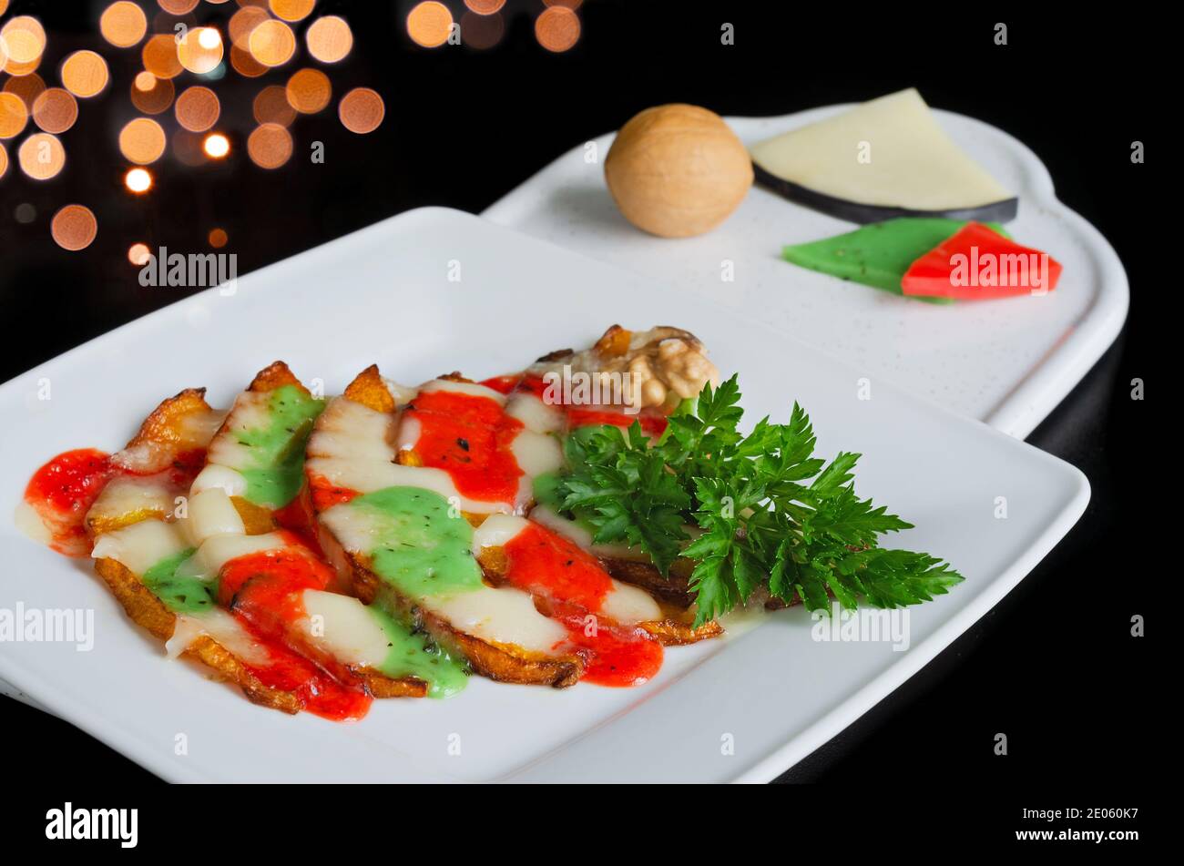 Zucca fritta con formaggio fuso, erbe e noci su un piatto, fondo nero. Messa a fuoco selettiva Foto Stock