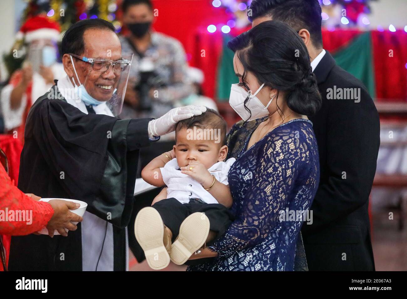 Medan, Sumatera del Nord, Indonesia. 26 Dicembre 2020. Un prete che indossa uno scudo facciale come misura contro la diffusione di Covid19 è visto posare la mano su un bambino durante la cerimonia di battesimo dei bambini della congregazione cristiana alla chiesa protestante di Batak Karo a Medan. Credit: Kartik Byma/SOPA Images/ZUMA Wire/Alamy Live News Foto Stock