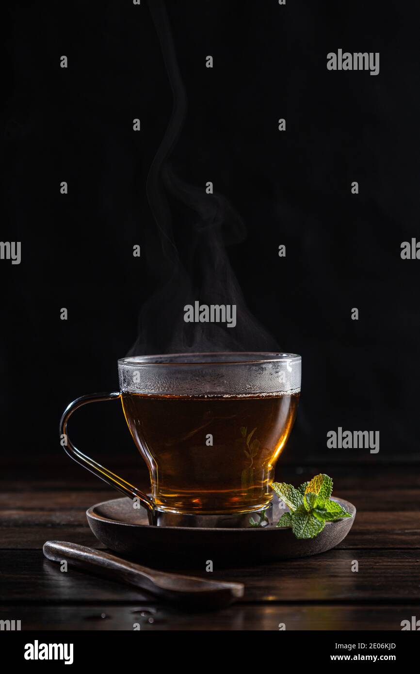 Infusione di menta piperita in vetro cristallino con foglie di menta fresca, su base di legno scuro rustico. Foto Stock