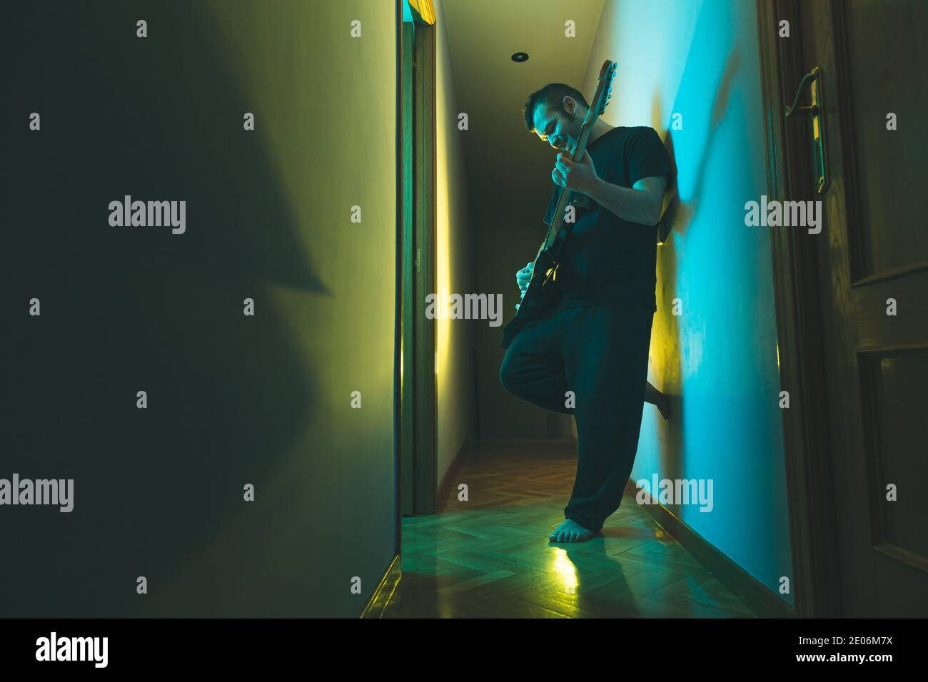 Uomo caucasico che suona la chitarra elettrica a casa. Illuminazione colorata. Foto Stock