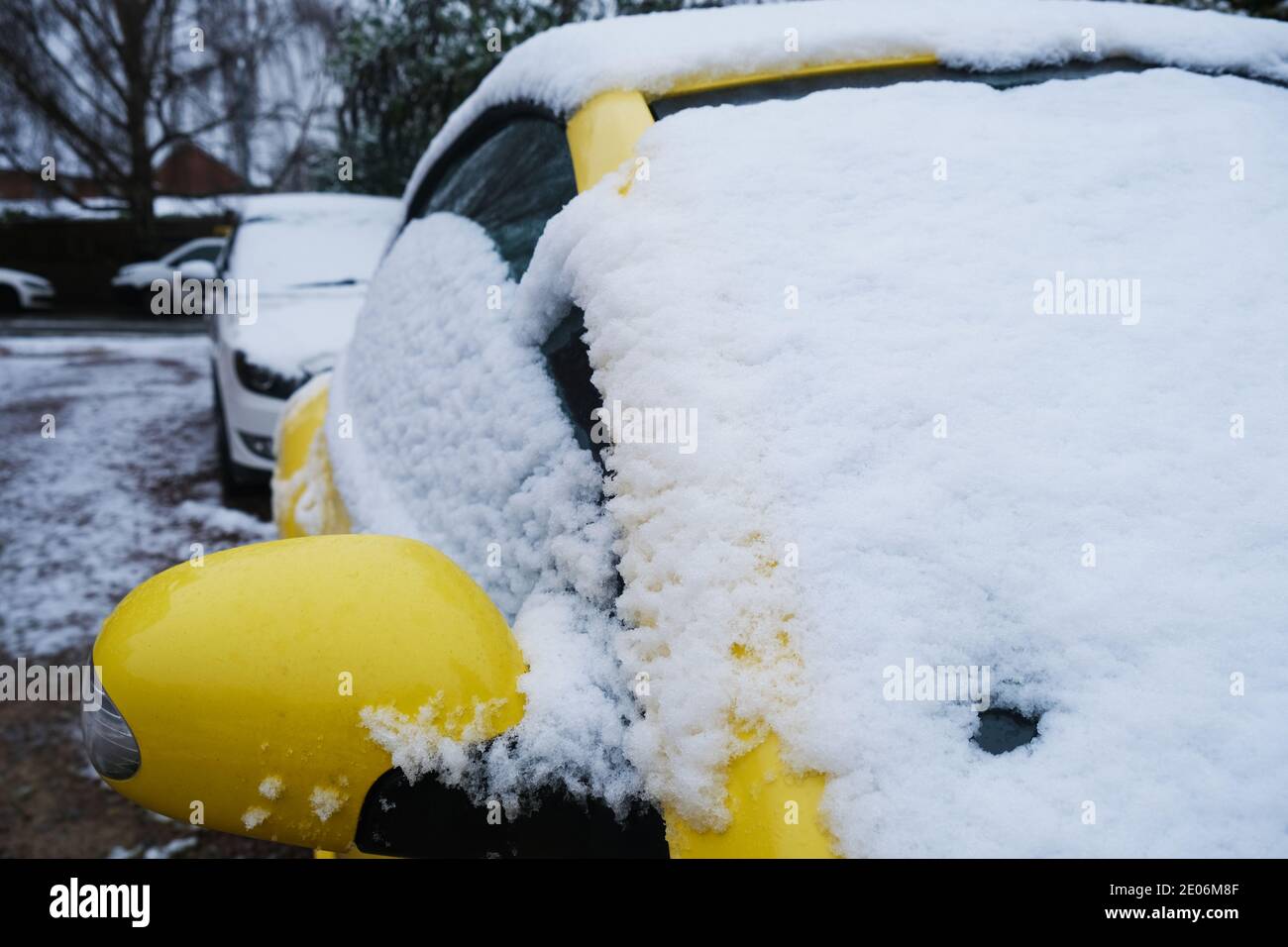 Neve fresca che ricopre il parabrezza e lo specchio retrovisore dell'auto, con la strada ghiacciata sullo sfondo. Foto Stock